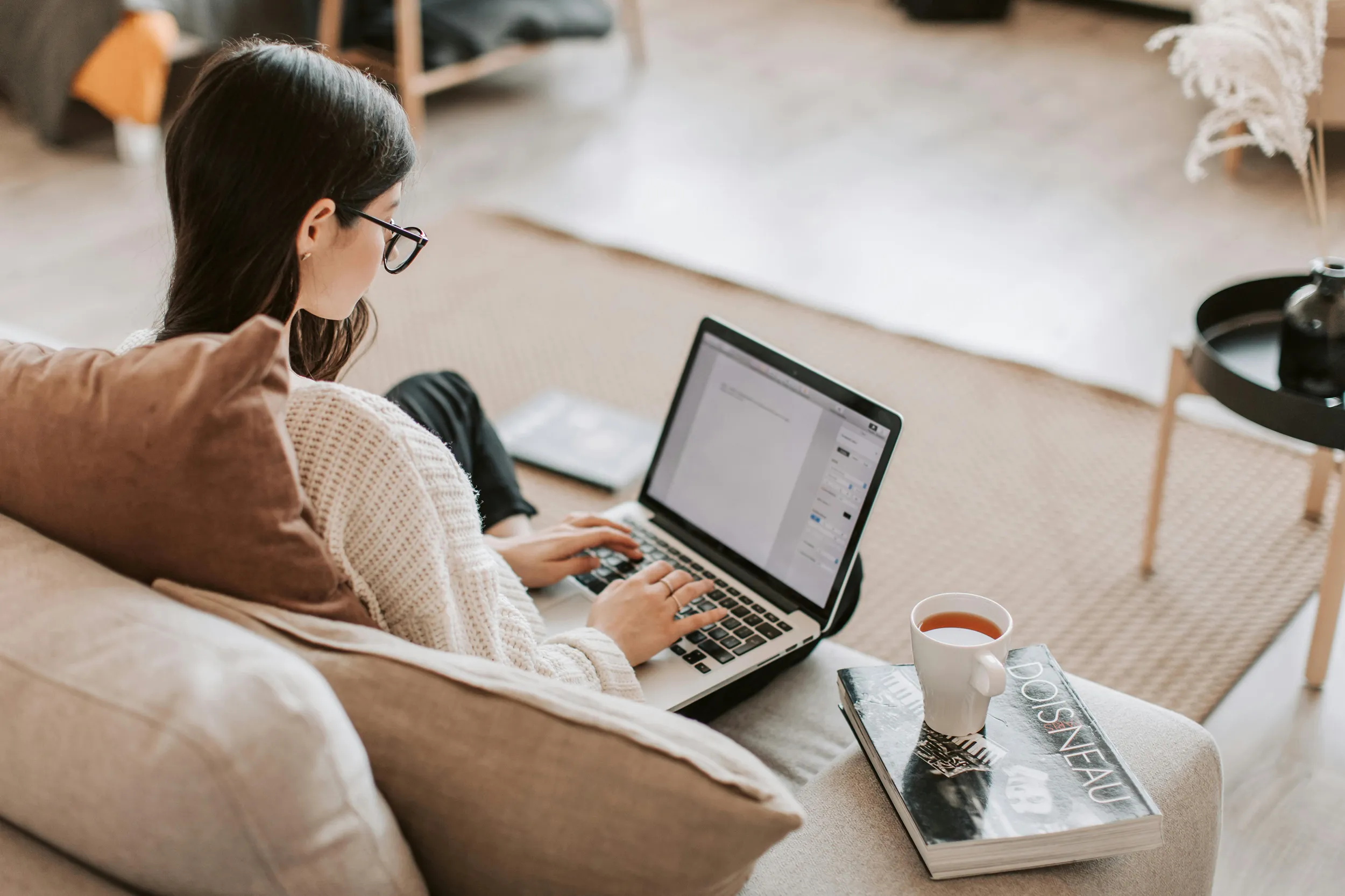 Woman working on laptop from cozy living room couch, relaxed remote work lifestyle
