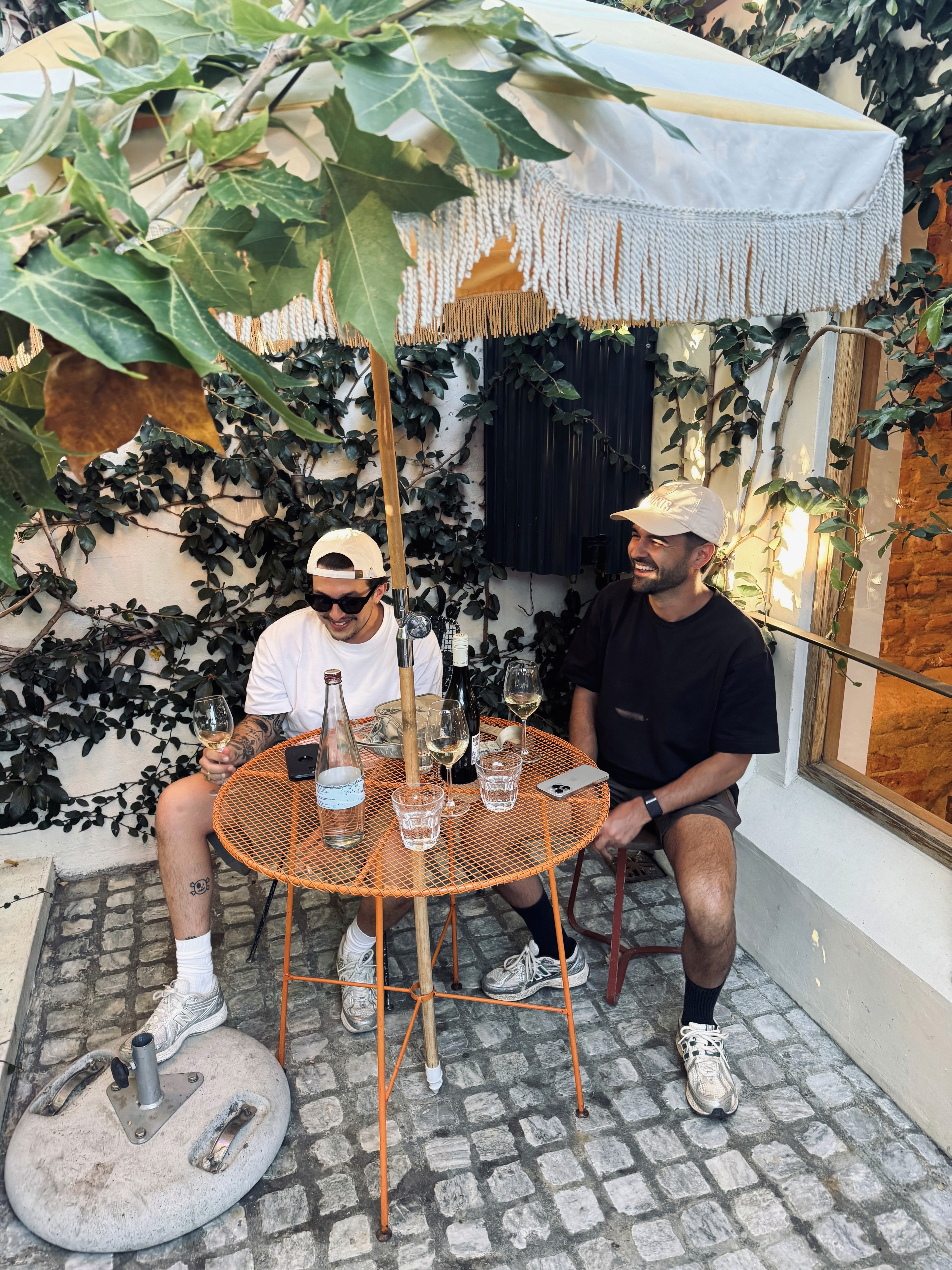 A view from an airplane window shows the aircraft's wing with a golden hue reflecting the setting sun, against a serene backdrop of fluffy clouds and a clear sky.