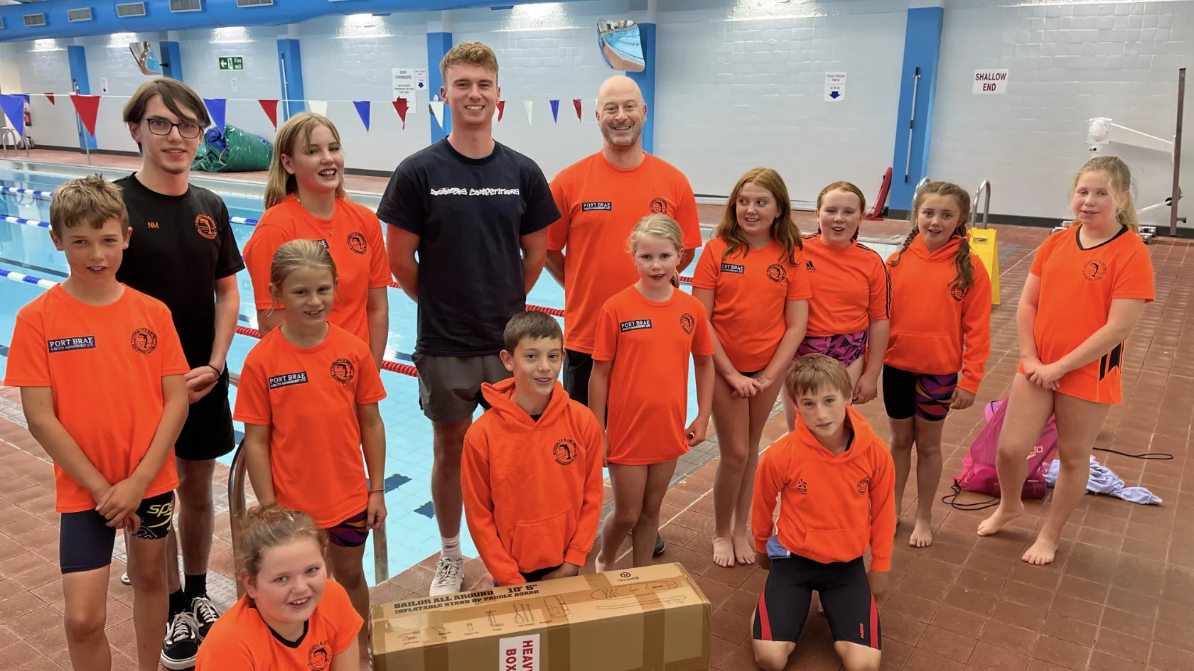 Jack Crowe of Borders Competitions presents a prize to young swimmers and coaches beside an indoor pool.