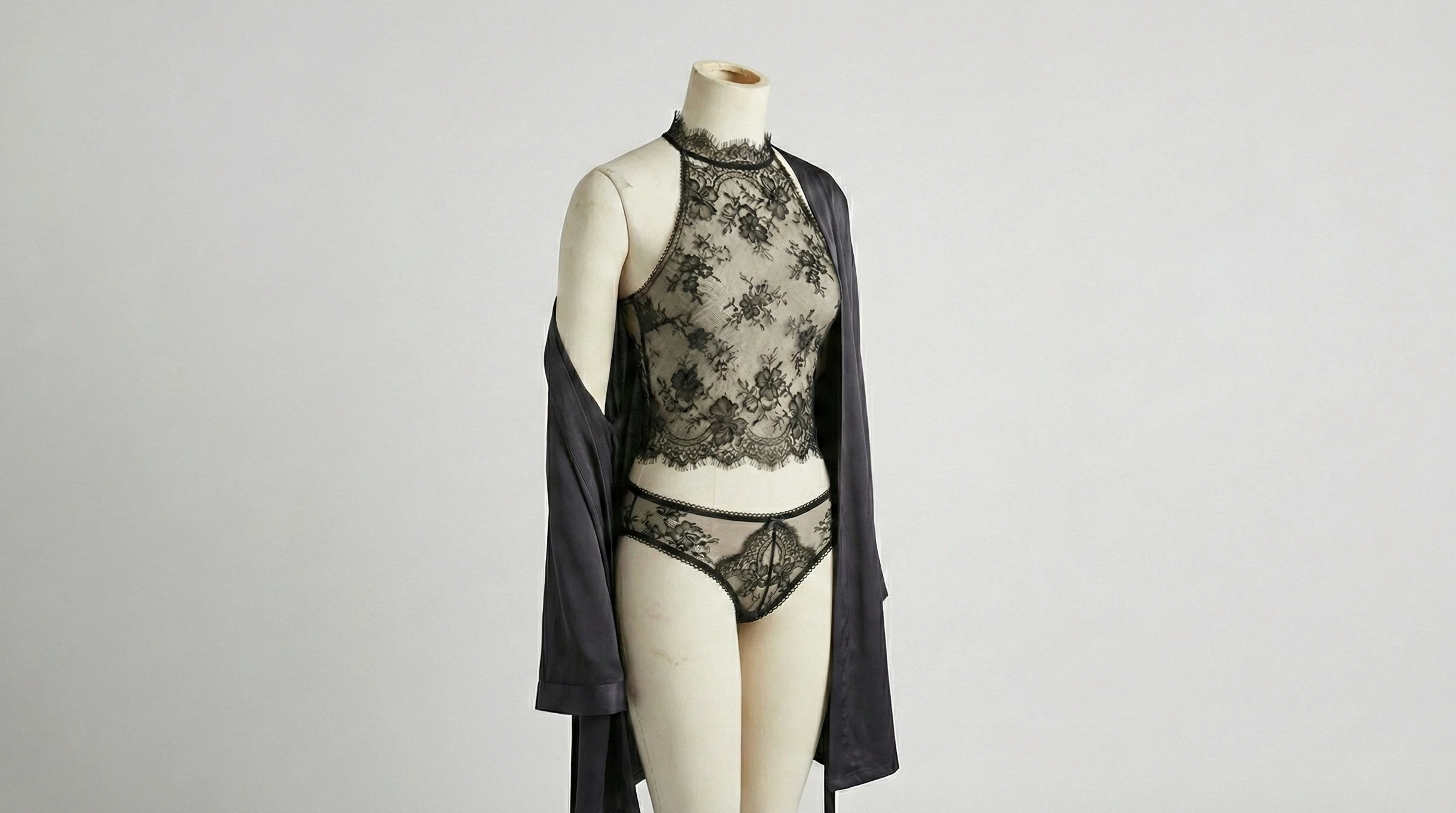 Black lace bodysuit displayed on a mannequin with a dark robe draped over the shoulders.