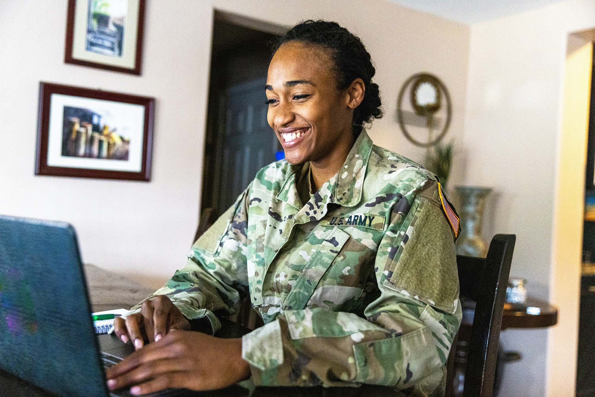 A woman in a U.S. Army uniform smiles while using a laptop.