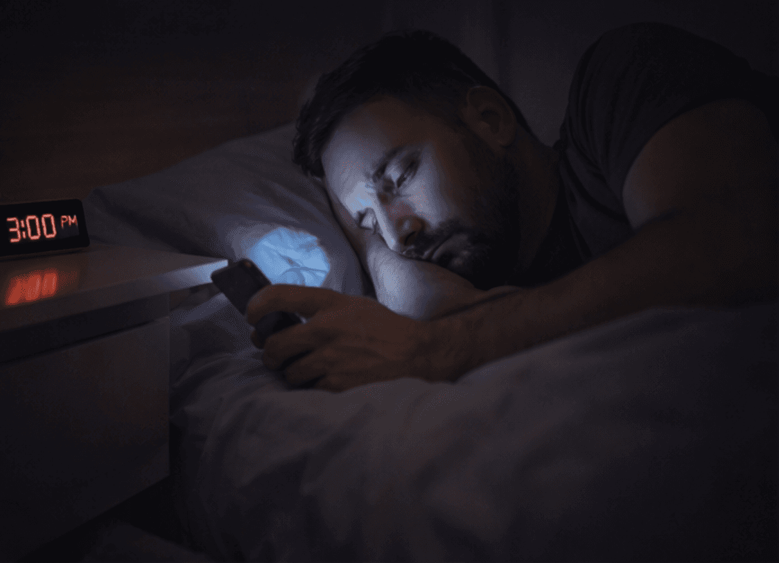 ein mann liegt im bett und schau traurig auf sein handy