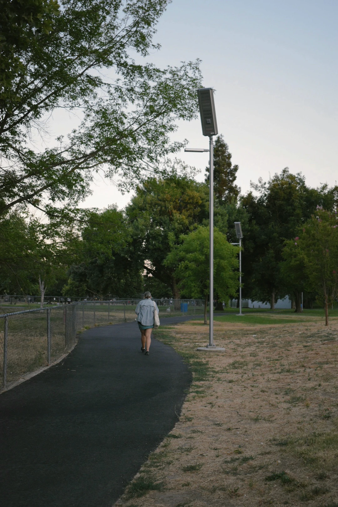 A woman walks along a sidewalk with a Leadsun solar path light to her right hand side.