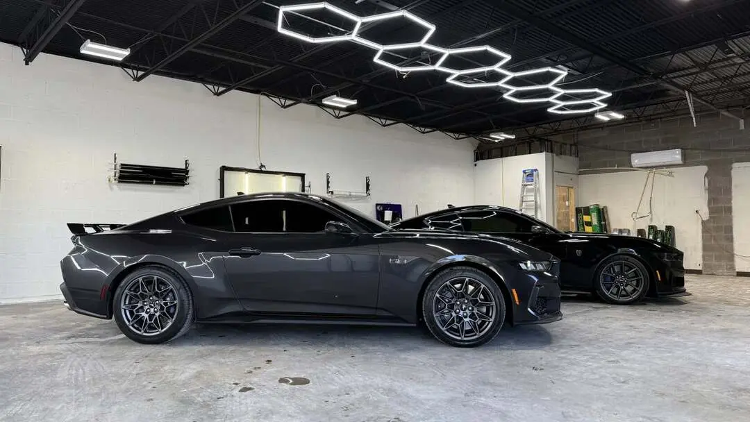 Two black cars under white lights in a detailing shop