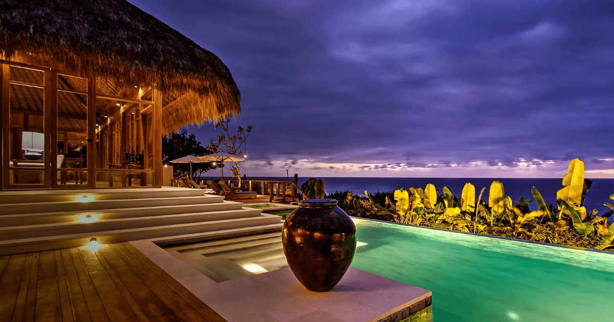 A luxurious villa with warm lighting and a pool overlooking the ocean