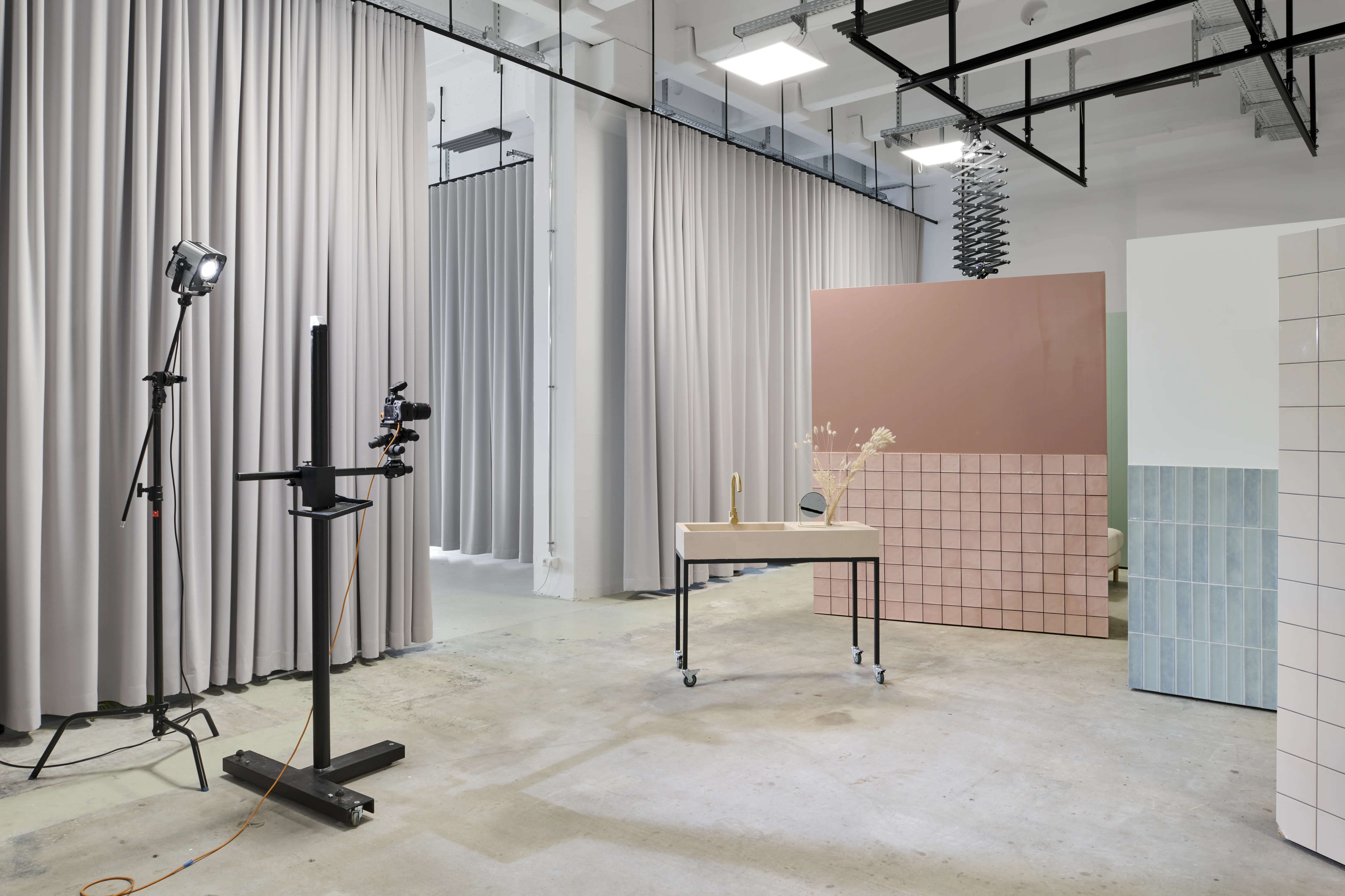 Photo set at the FLACONI CONTENT STUDIO with a studio lamp and camera rig, a rolling table in front of pink tiled backdrop walls and grey curtain dividers.