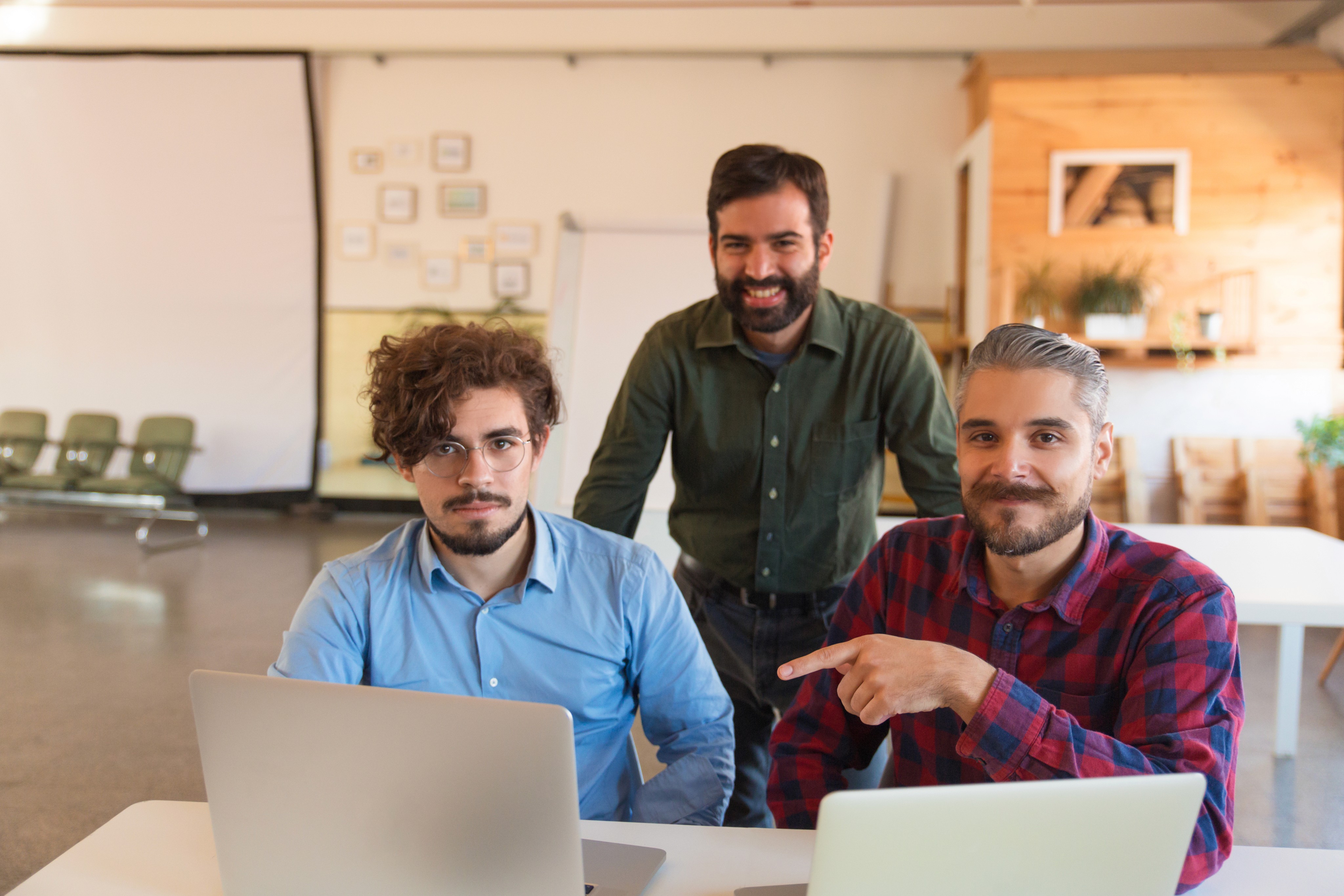 Three men working on laptops in a casual office, with one man pointing at a screen.