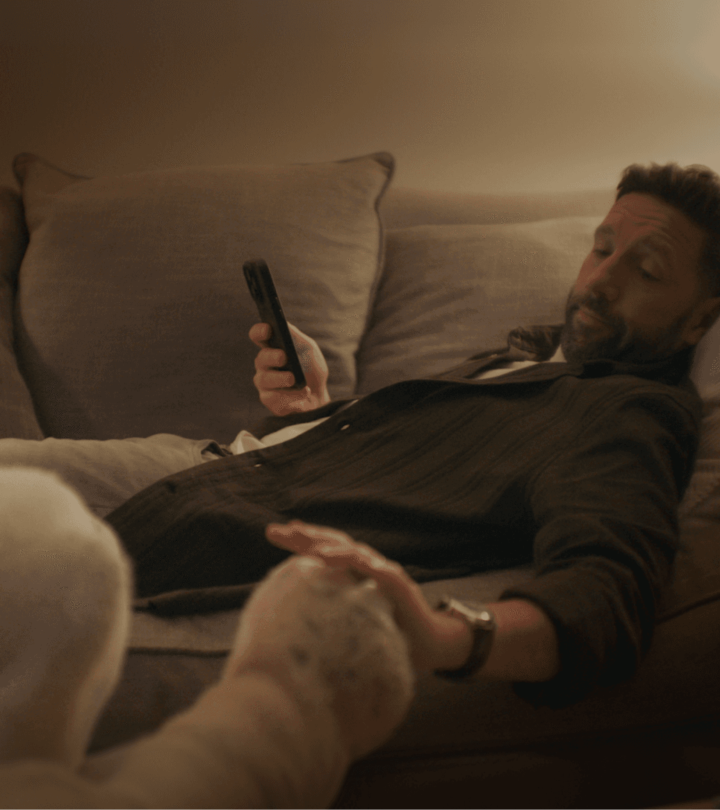 Man reclining on a couch watching TV while high-fiving a familiar beside him