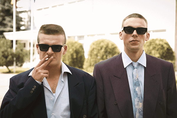 Two lead characters from Southern Chronicles (Pietinia Kronikas) standing confidently in sunglasses — a bold 90s-inspired Nordic comedy-drama.