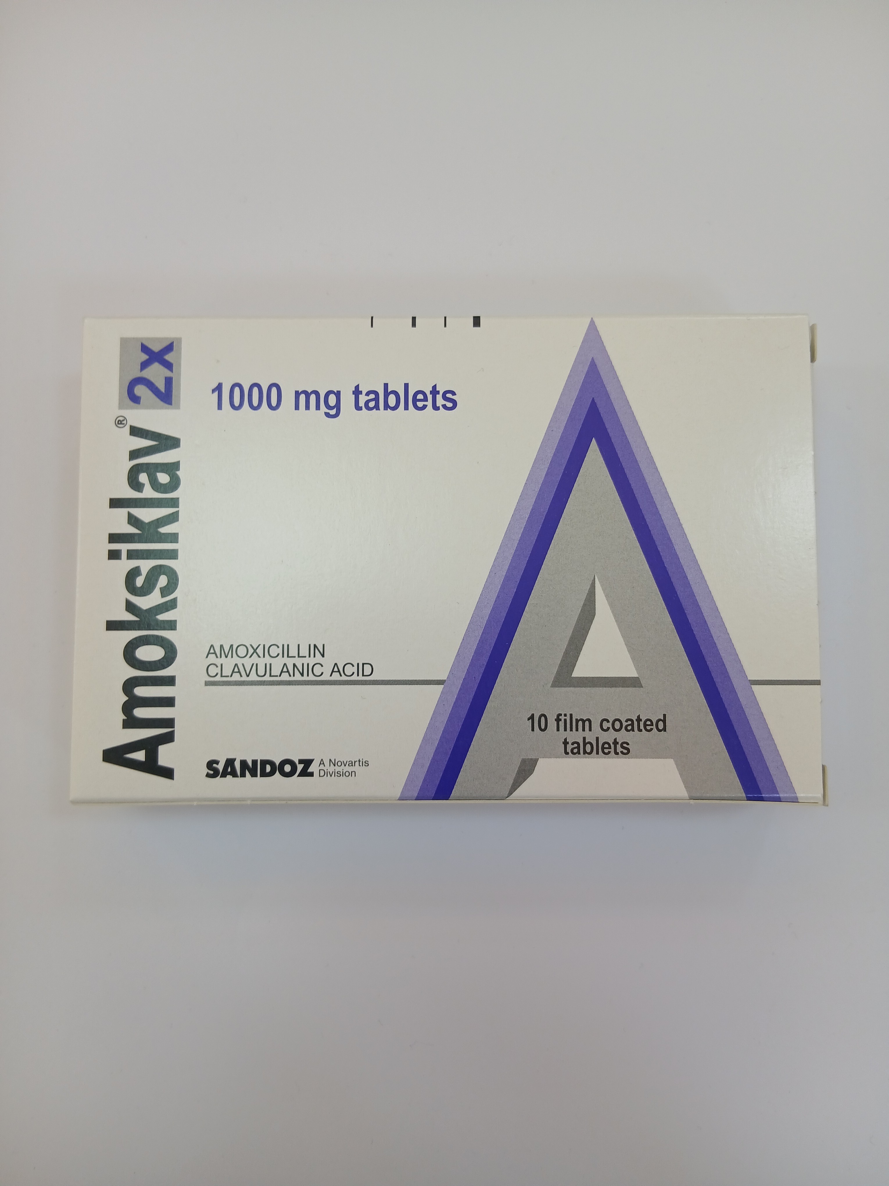 White cardboard packaging displays a large purple triangular graphic with a white border, containing a blister pack of ten light-colored film-coated tablets.
