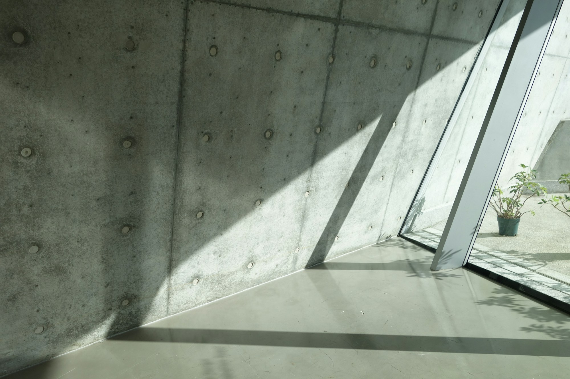 Raking sunlight across tie-holed concrete beside a slanted glazed wall