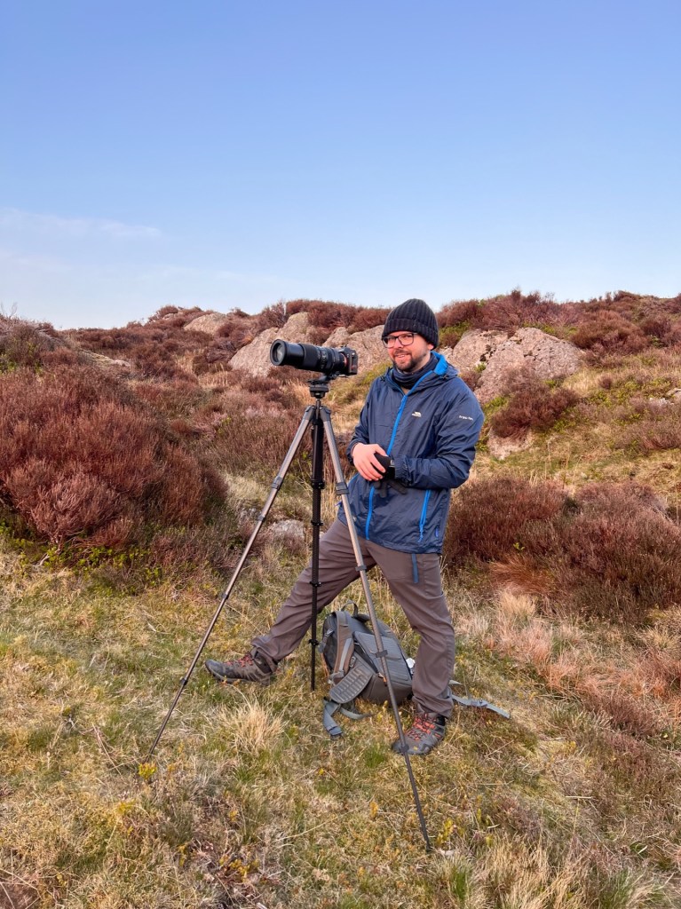 Martin stood on Holme Fell behind his camera that is on a tripod.