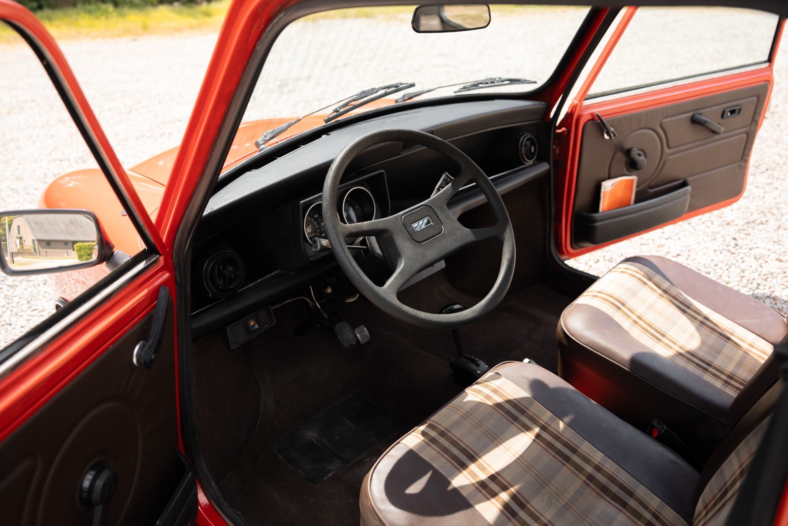Interior of a vintage car featuring a steering wheel, gear shift, and classic dashboard details in red and black.