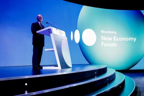 person discussing while standing in front of a large screen in front of people inside dim-lighted room