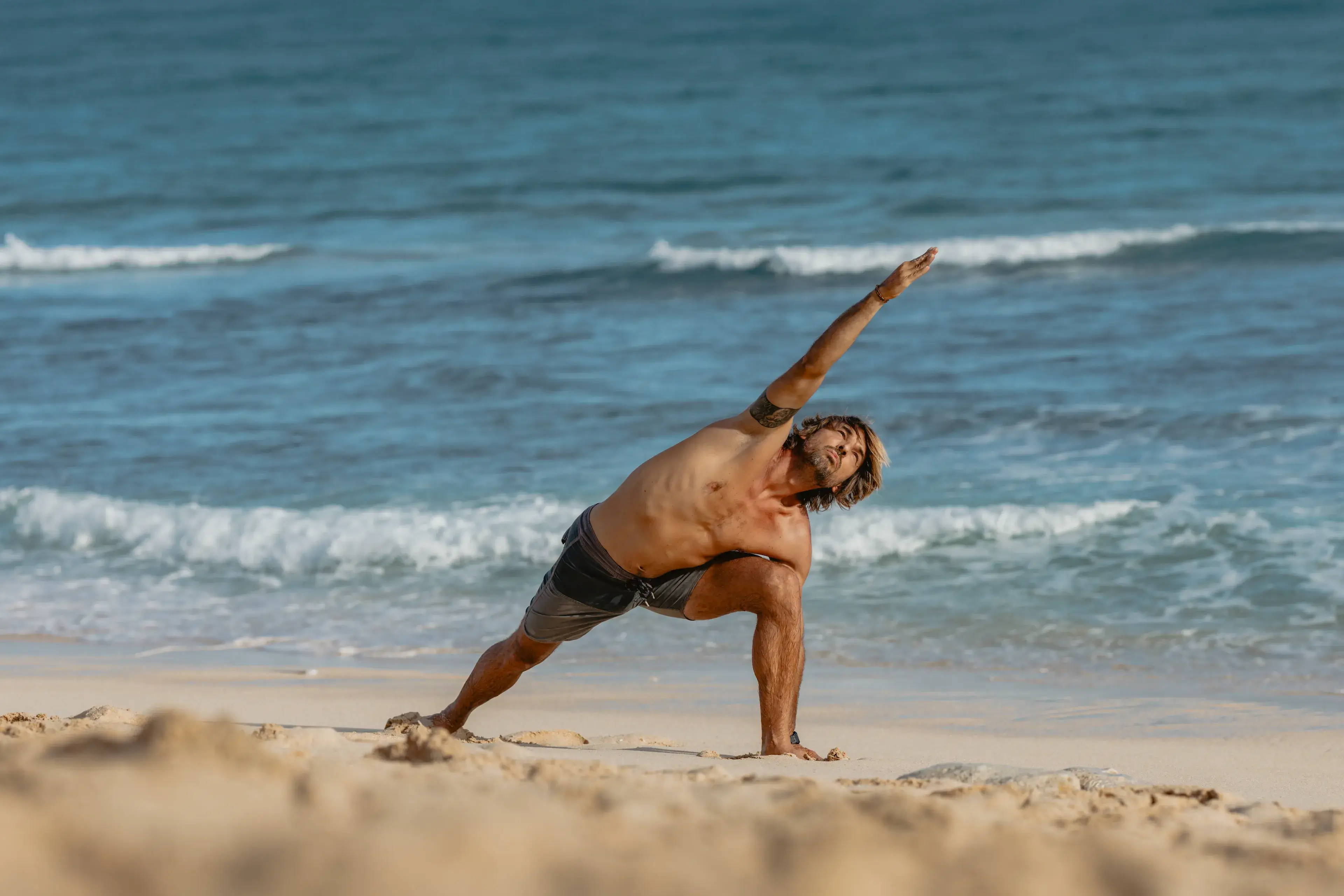 Male yoga student practicing extended side angle pose on the beach for the 200hr Vinyasa yoga training in Bali