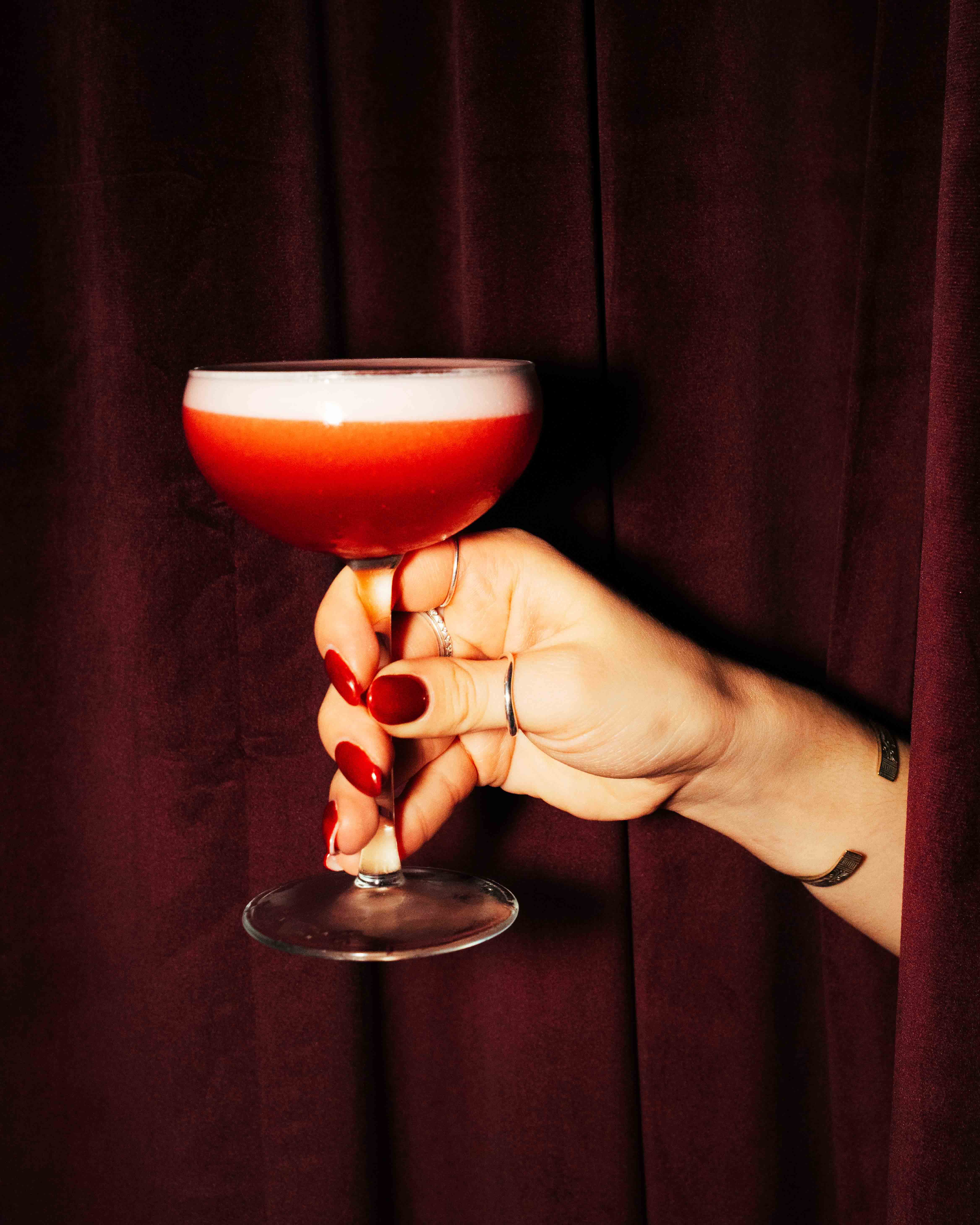 Person with a mustache wearing a black t-shirt carrying a tall stack of pizza boxes inside a dimly lit bar or restaurant.