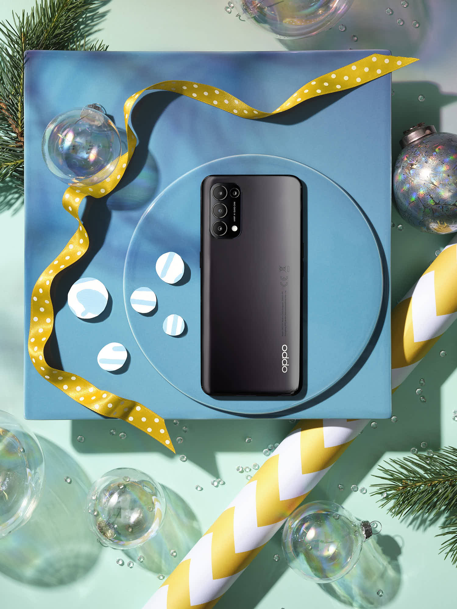 Smartphone on blue gift box with Christmas decorations and yellow ribbon.