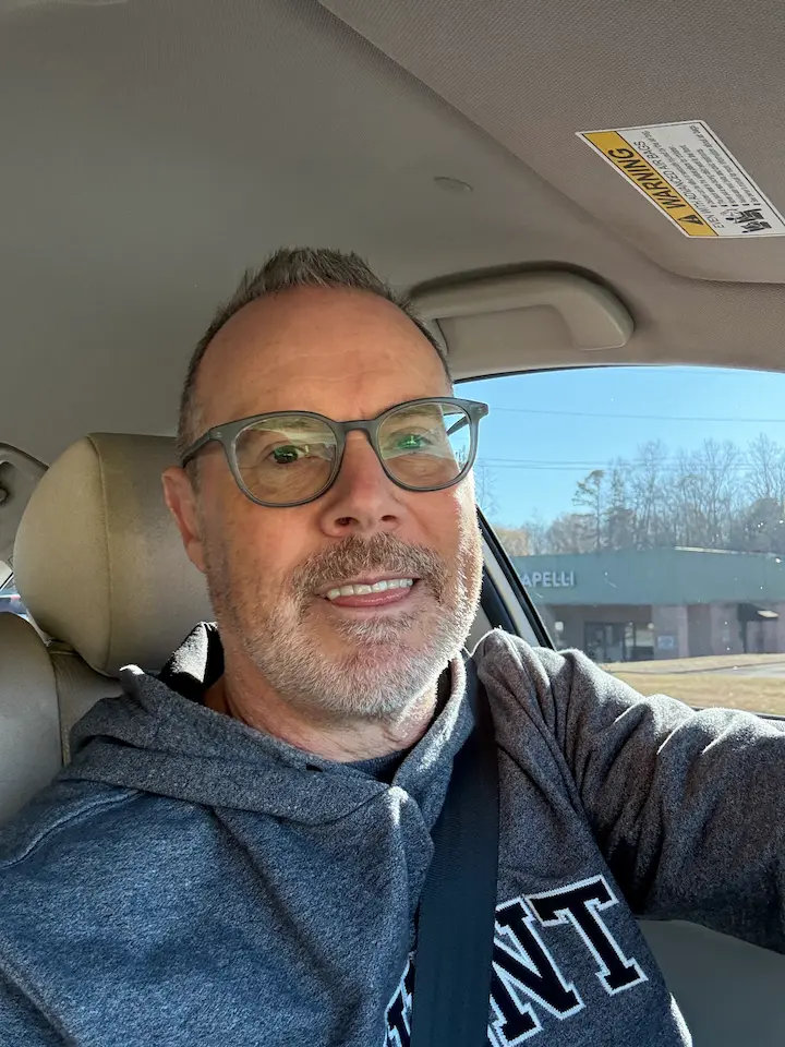 Stu driving his Honda Accord during the daytime while wearing glasses and a blue shirt, photographed from inside the car.