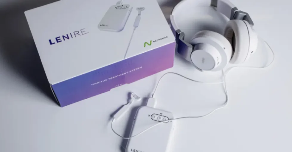 White headphones beside a white and purple box, with a small device partially visible in the foreground.