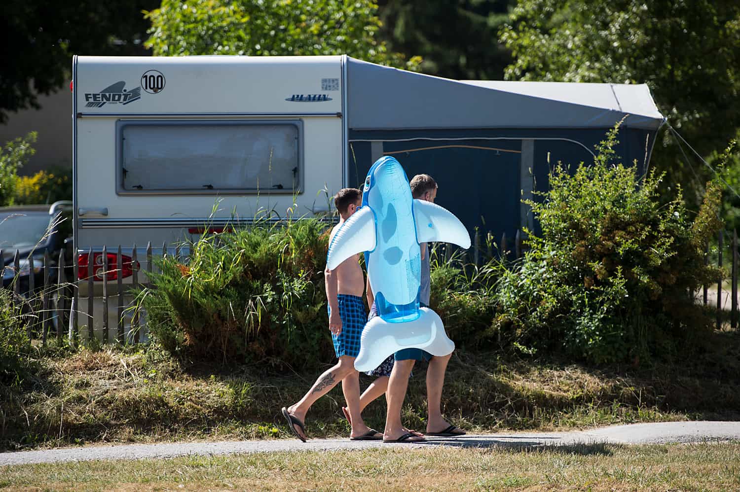 Kinder mit Schwimmtier laufen an einem Wohnwagen vorbei