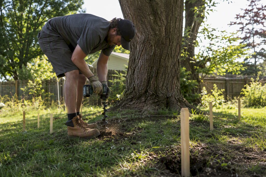 Deck builder drilling footing hole near tree