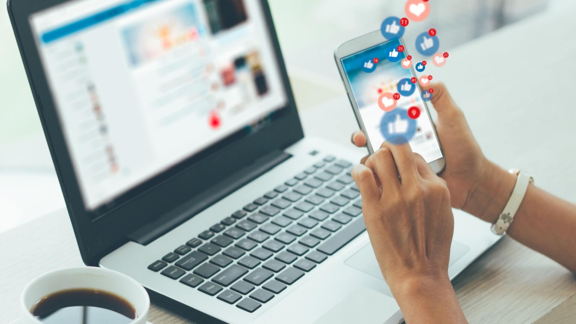 mano che maneggia cellulare con social dove escono simboli di like e cuori