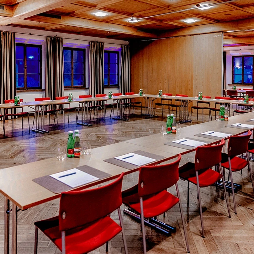 Ein Konferenzraum im Schloss Mattsee mit langen Tischen, roten Stühlen, Wasserflaschen & Schreibunterlagen.
