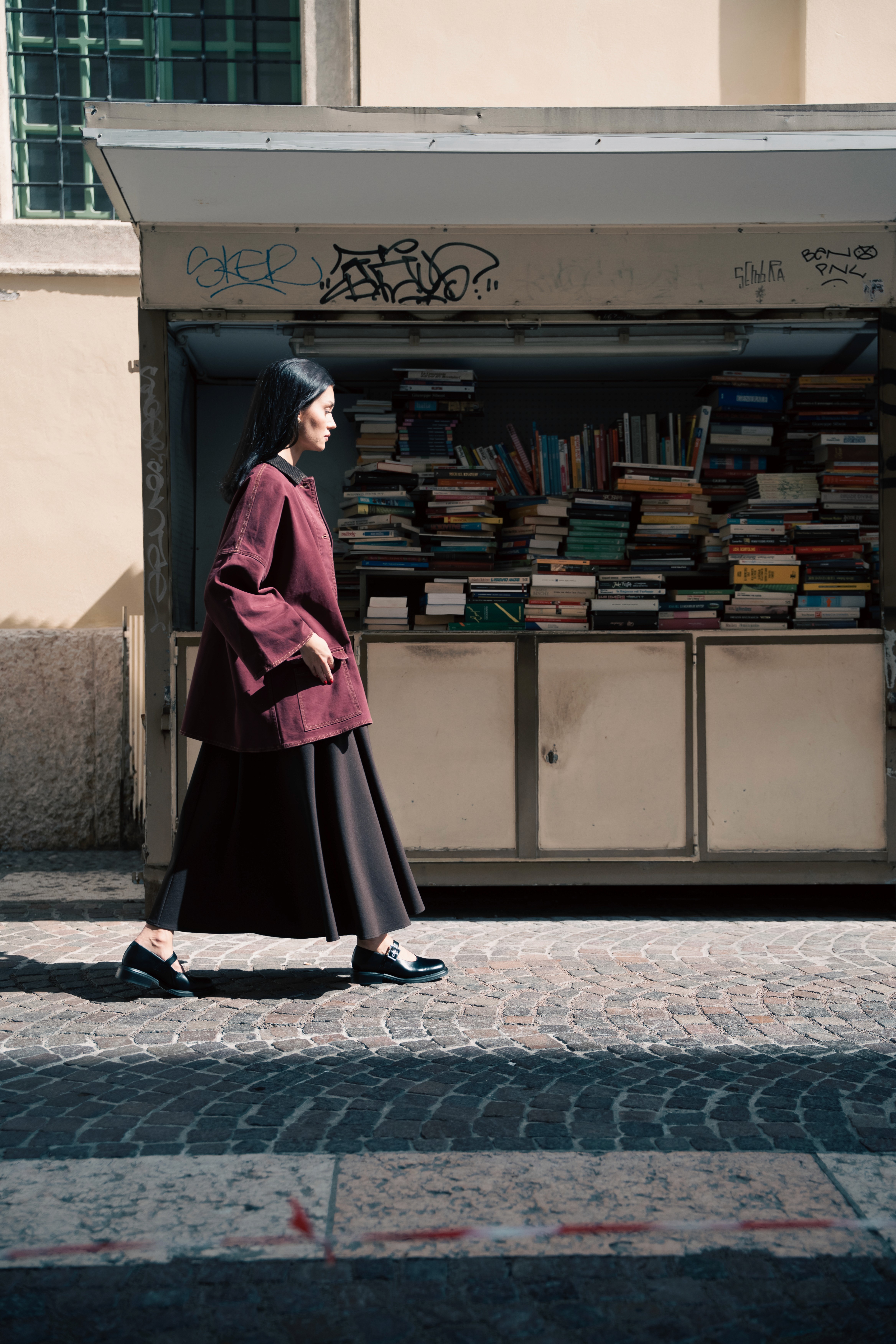 Femme marchant dans une rue pavée avec une jupe longue et un manteau rouge sombre