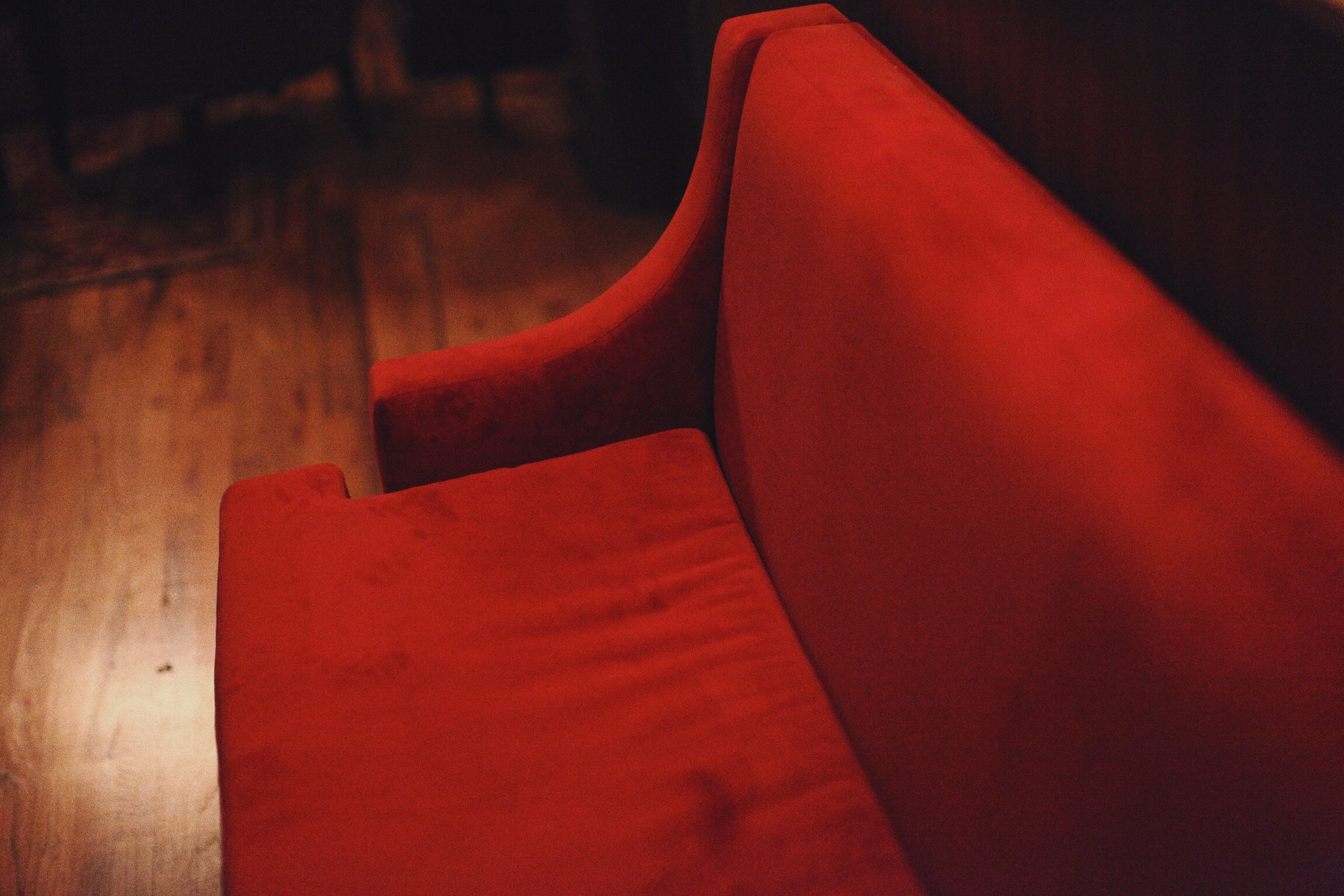 Close view of a red upholstered banquette beside a dark timber floor.