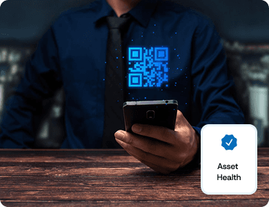 Person scanning a blue QR code with a smartphone, with a label reading “Asset Health,” representing live digital asset tracking.