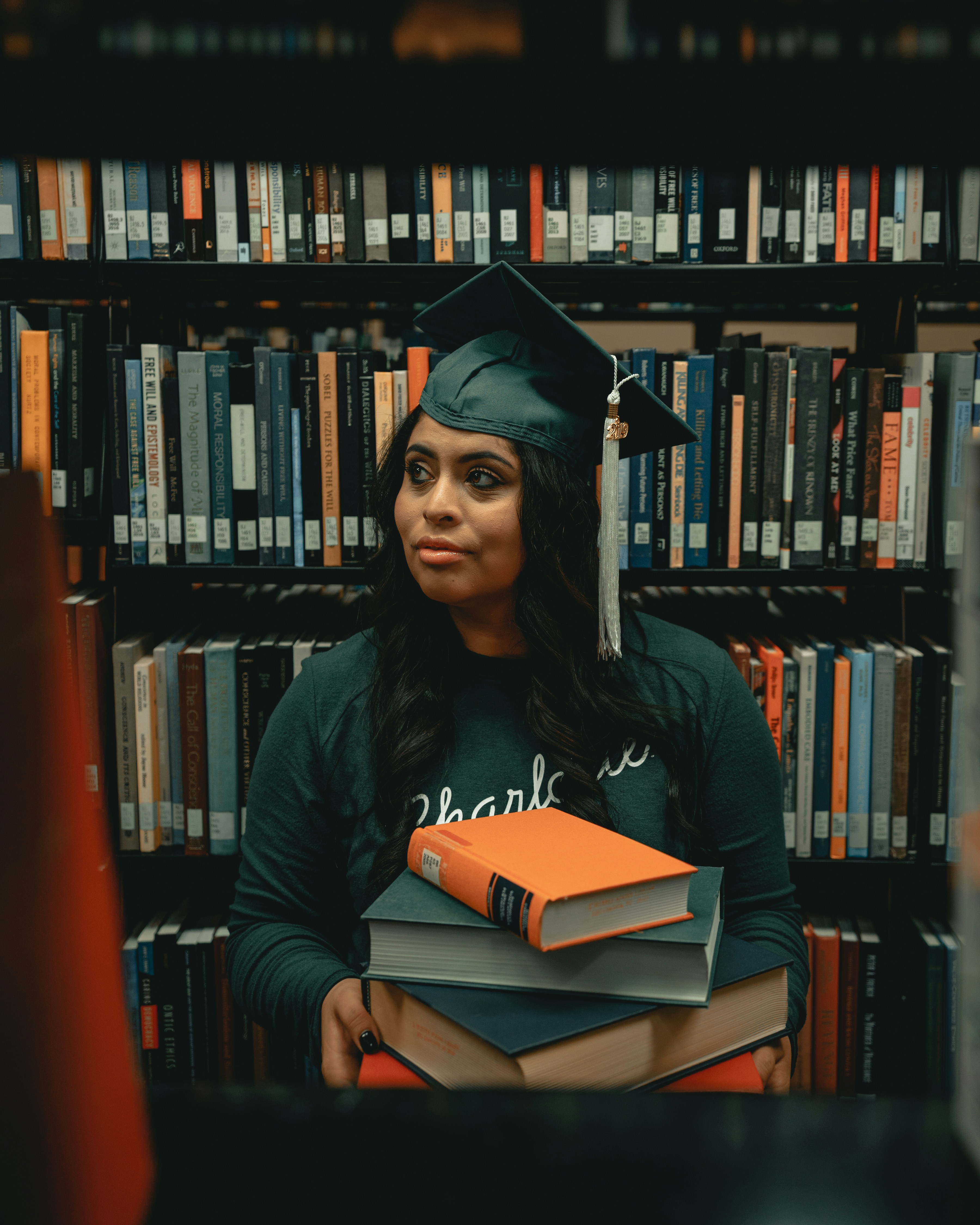 Black woman in a graduation outfit holding books in the library