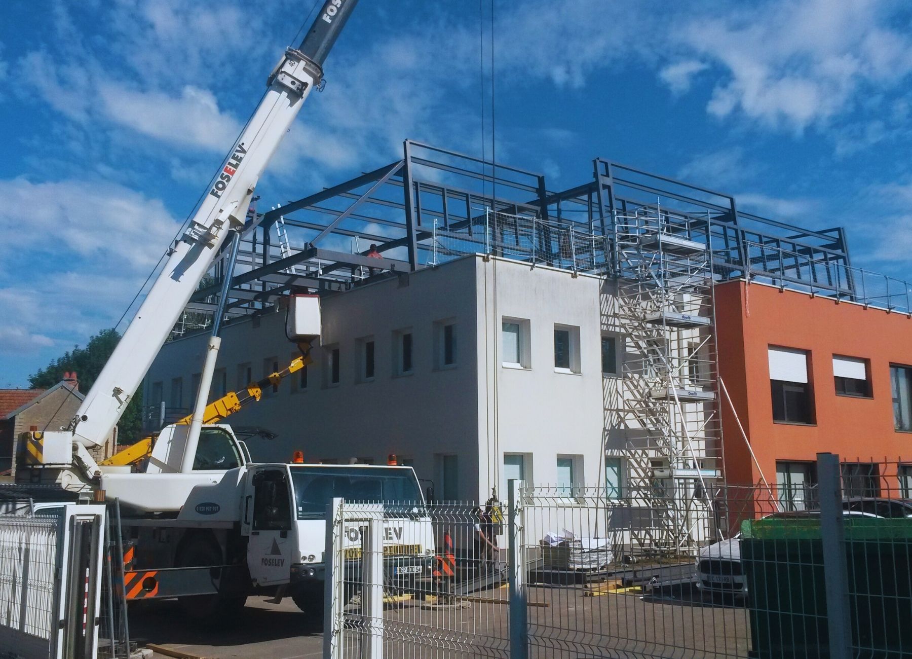 Montage d’une structure métallique avec grue sur un chantier de bâtiment tertiaire – façade blanche.