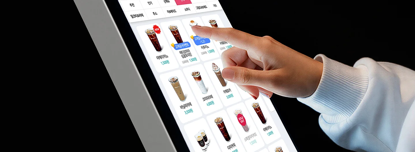다양한 음료 메뉴가 배열된 키오스크 화면에서 항목을 터치해 선택하는 장면