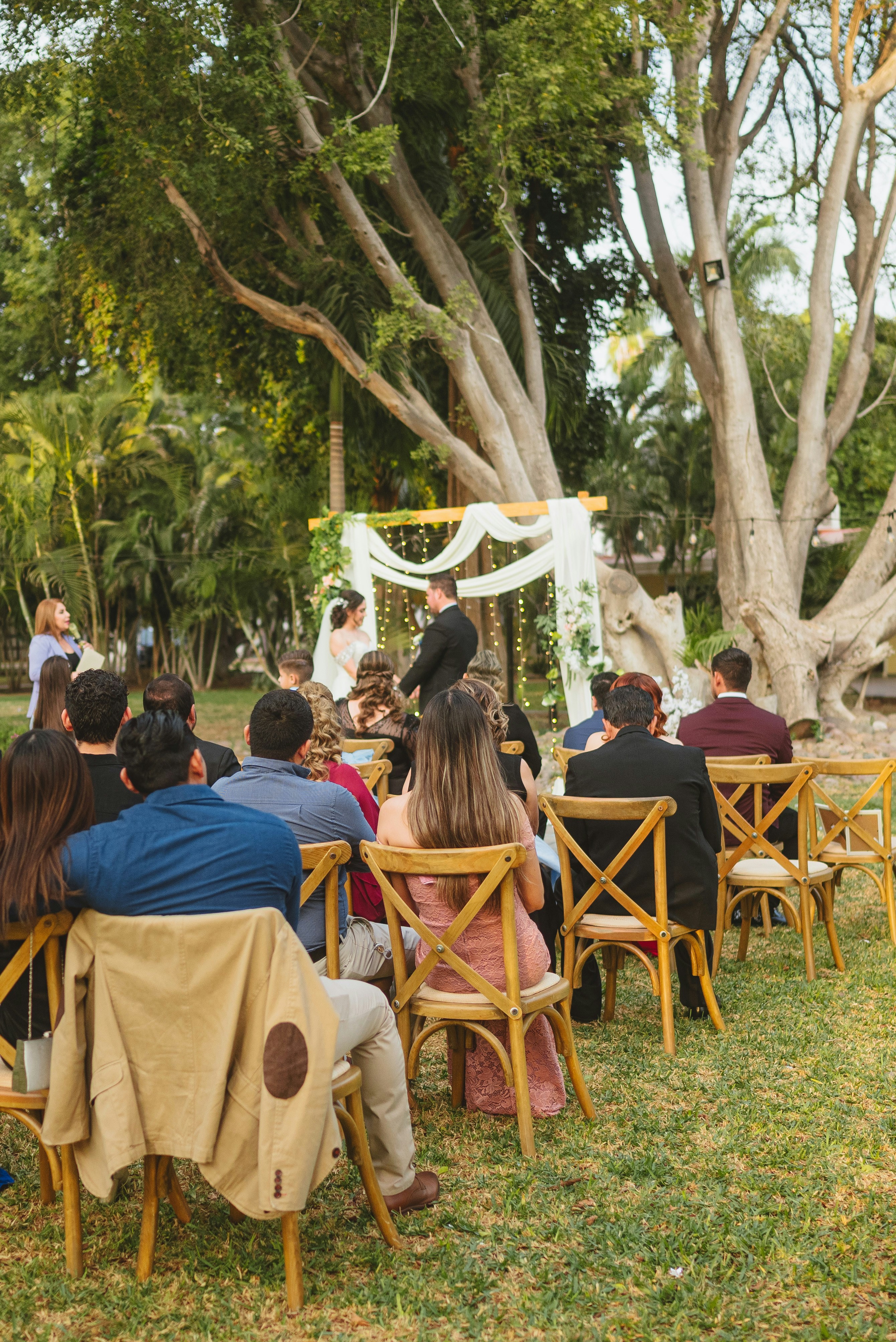 Wedding ceremony outdoors with guests seated on chairs.