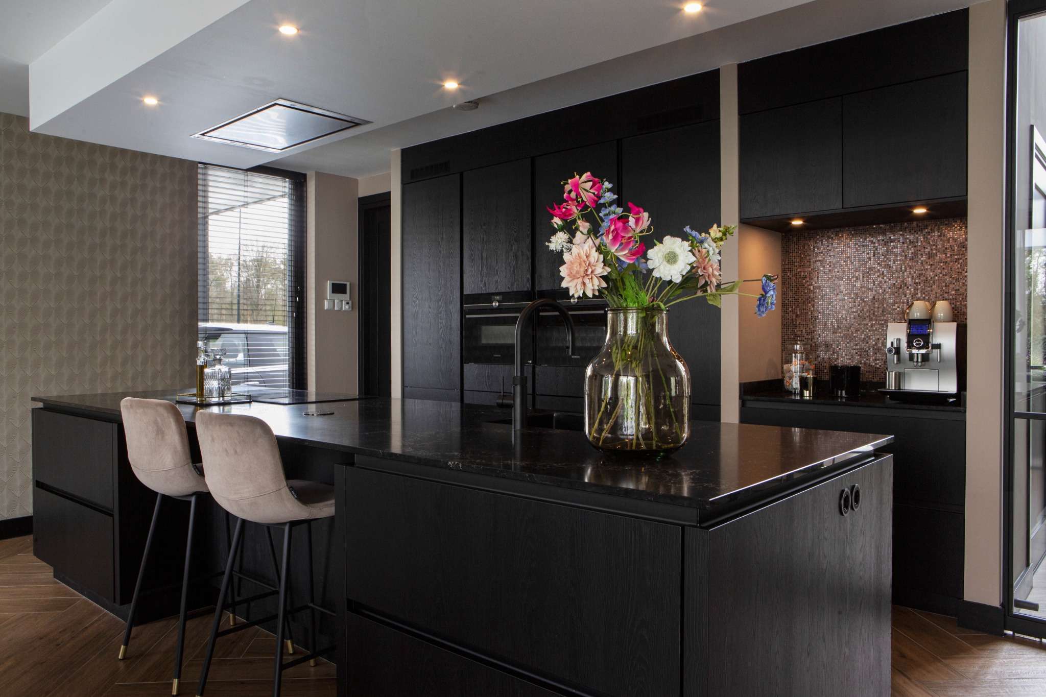Luxe donkere keuken met kookeiland, zwarte fronten en bloemenvaas op het werkblad.