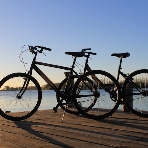 Dos bicicletas en un muelle de madera al atardecer, con vista a un lago tranquilo bajo un cielo azul claro.