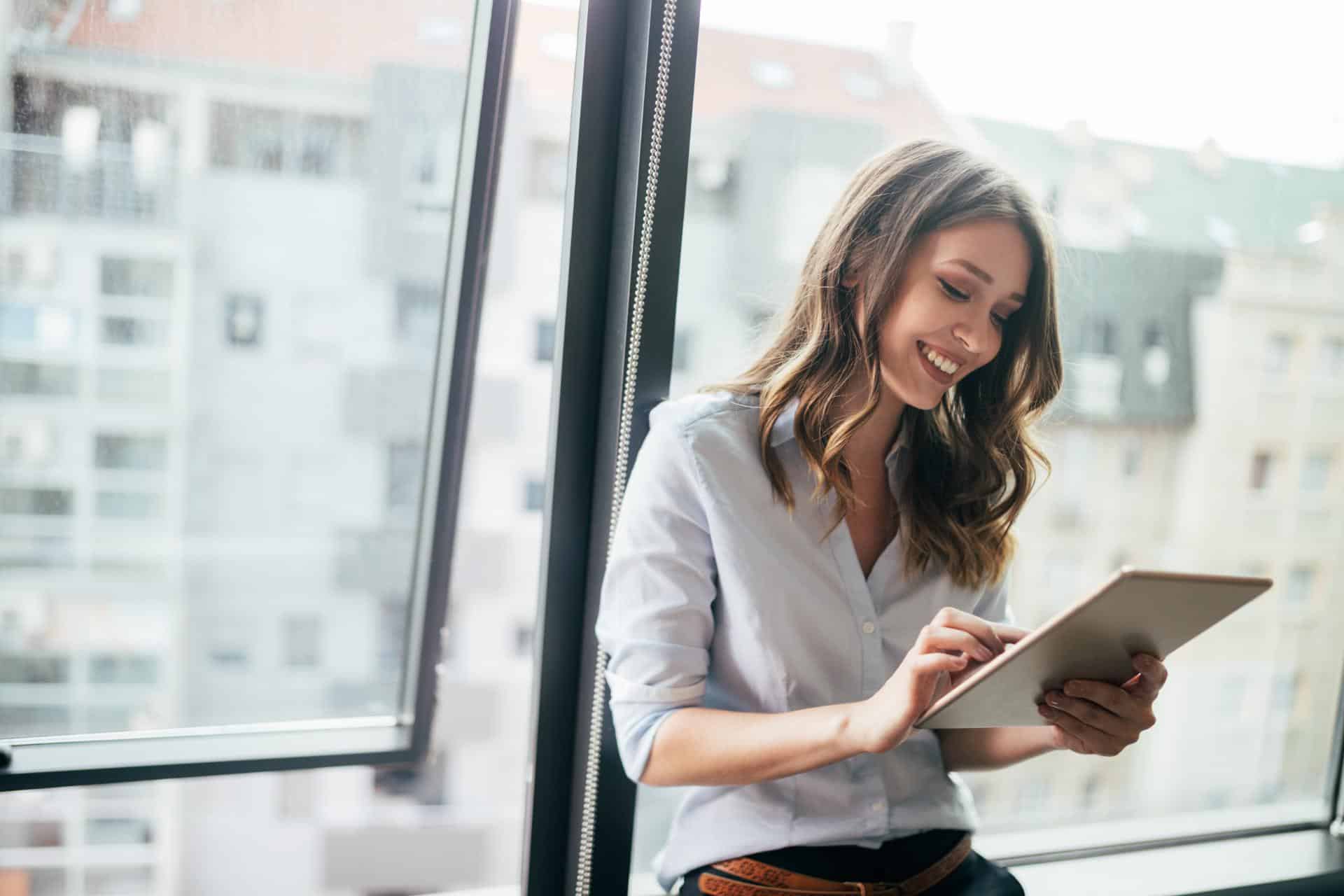Attractive businesswoman using a digital tablet while standing in front of windows