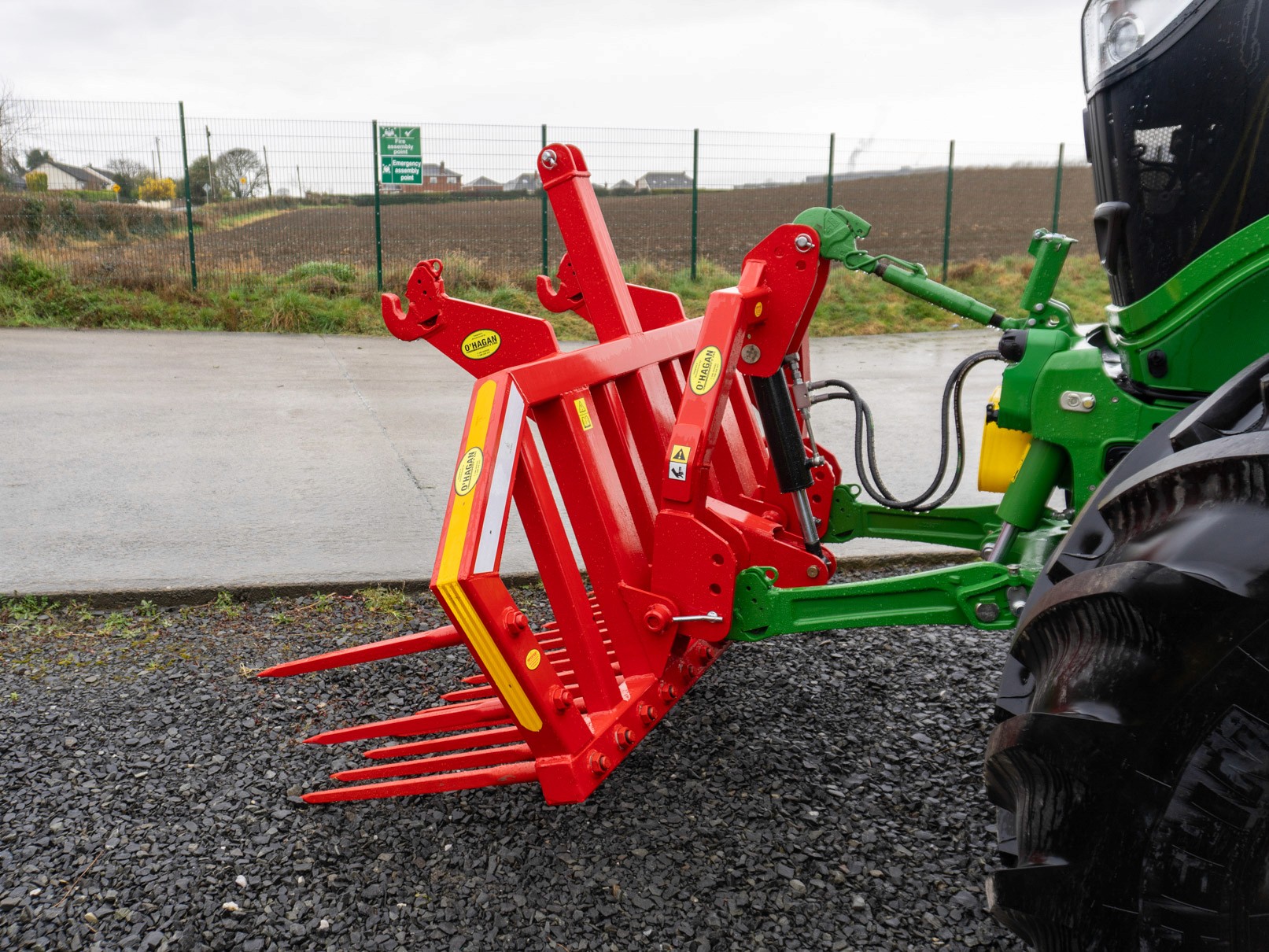 Red stone fork attached to a green john deere in a carpark with brown fields in the distance 