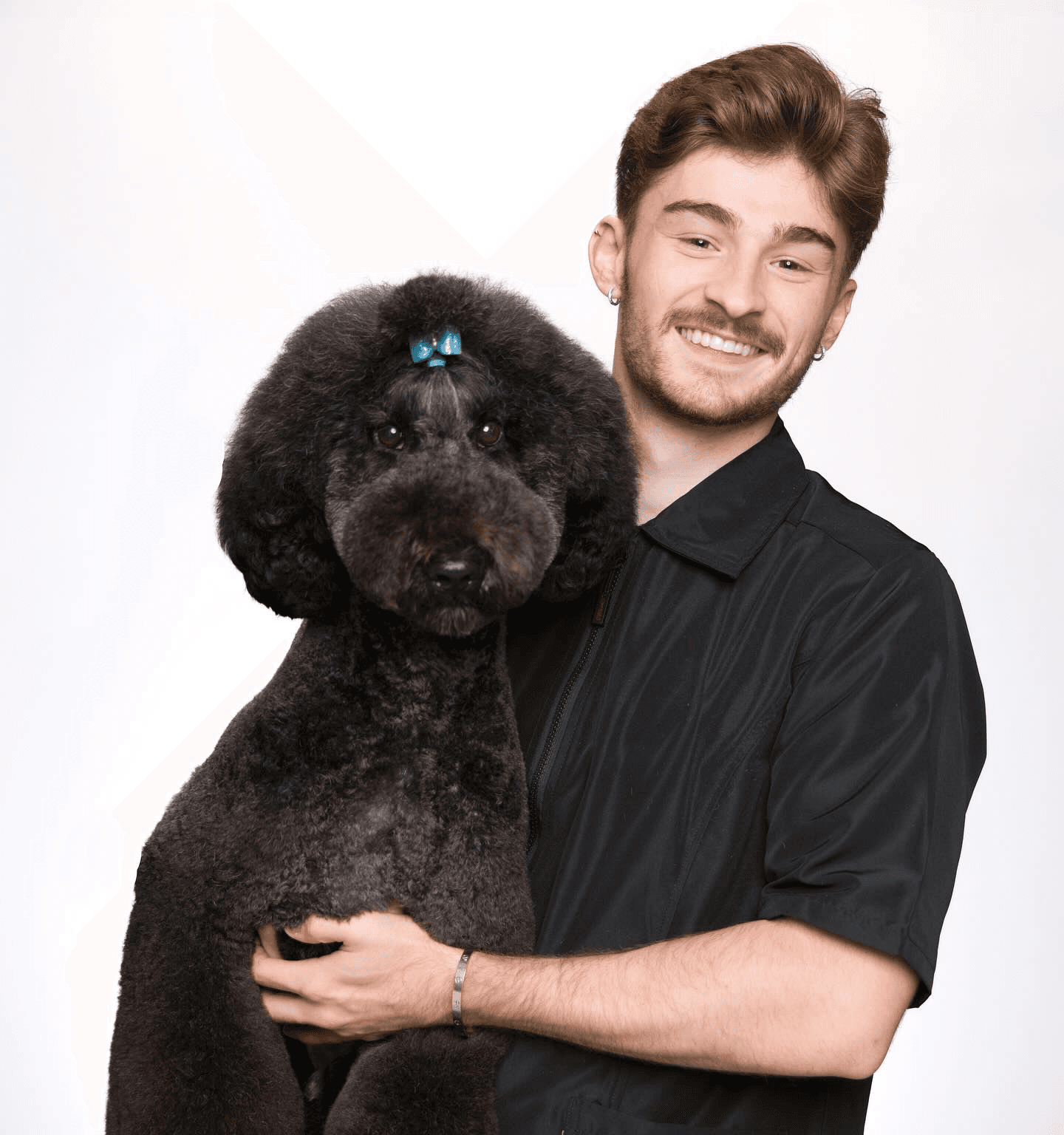 Portrait of Logan Rago holding a stylish black poodle with a blue bow to convey trust, care, and refined grooming expertise.