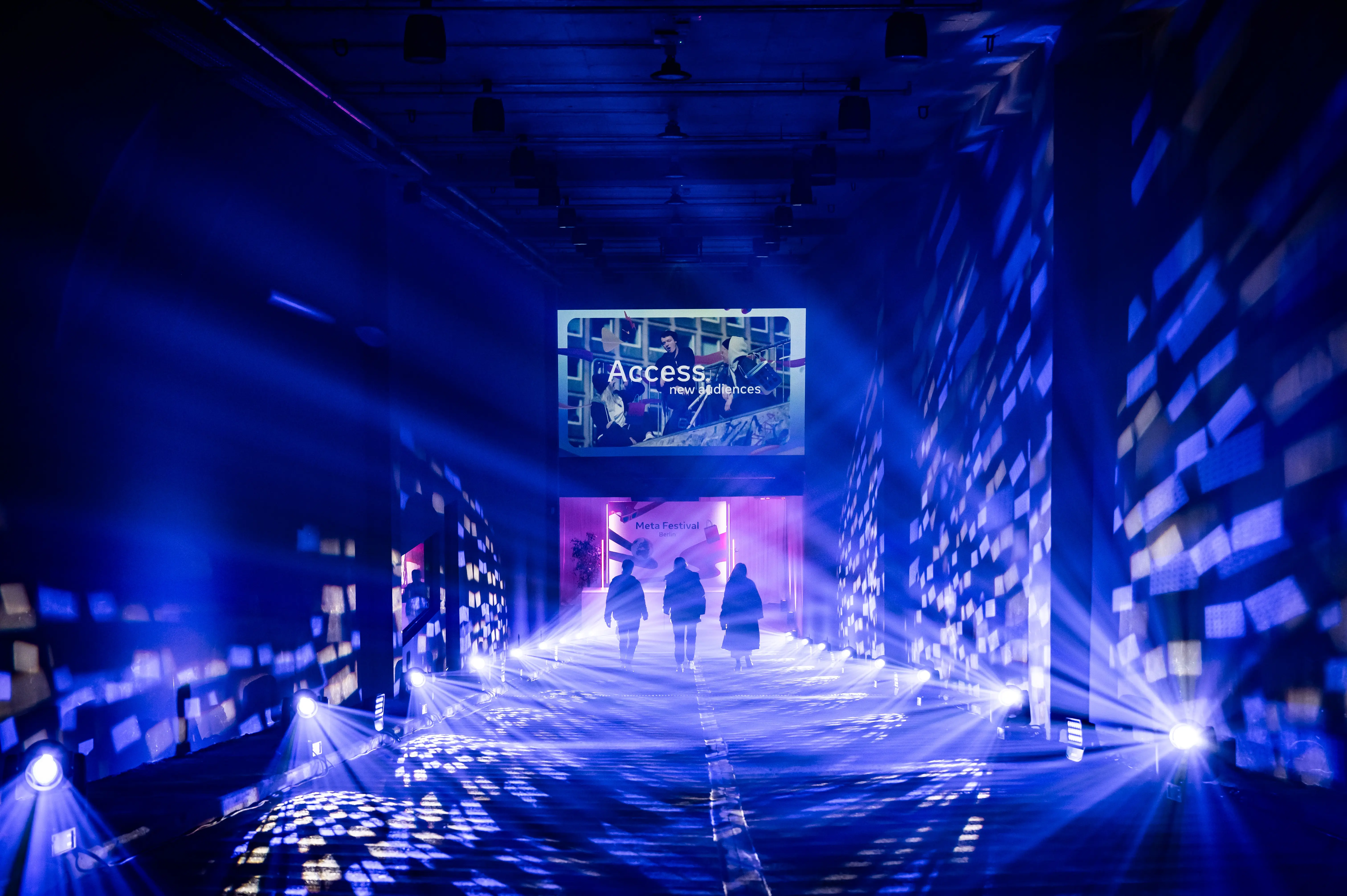 Three people in the blue sparkling light corridor under the Access projection.