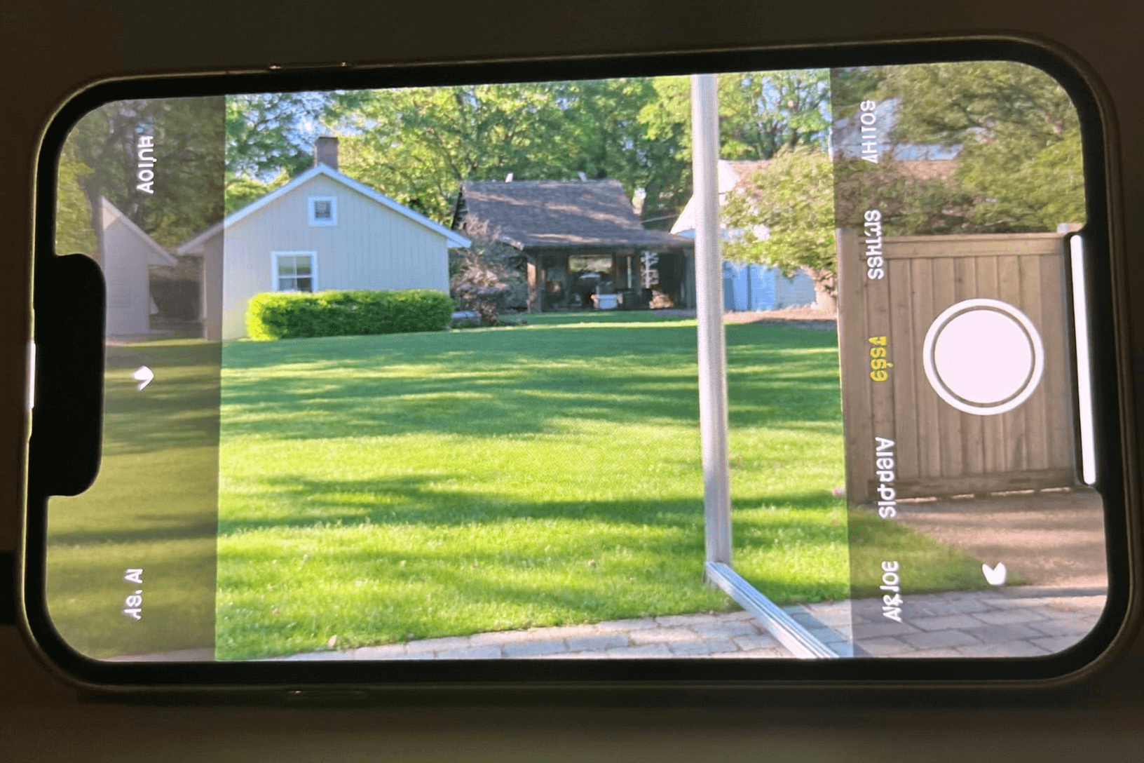 Phone screen showing a green sunny lawn and houses being photographed