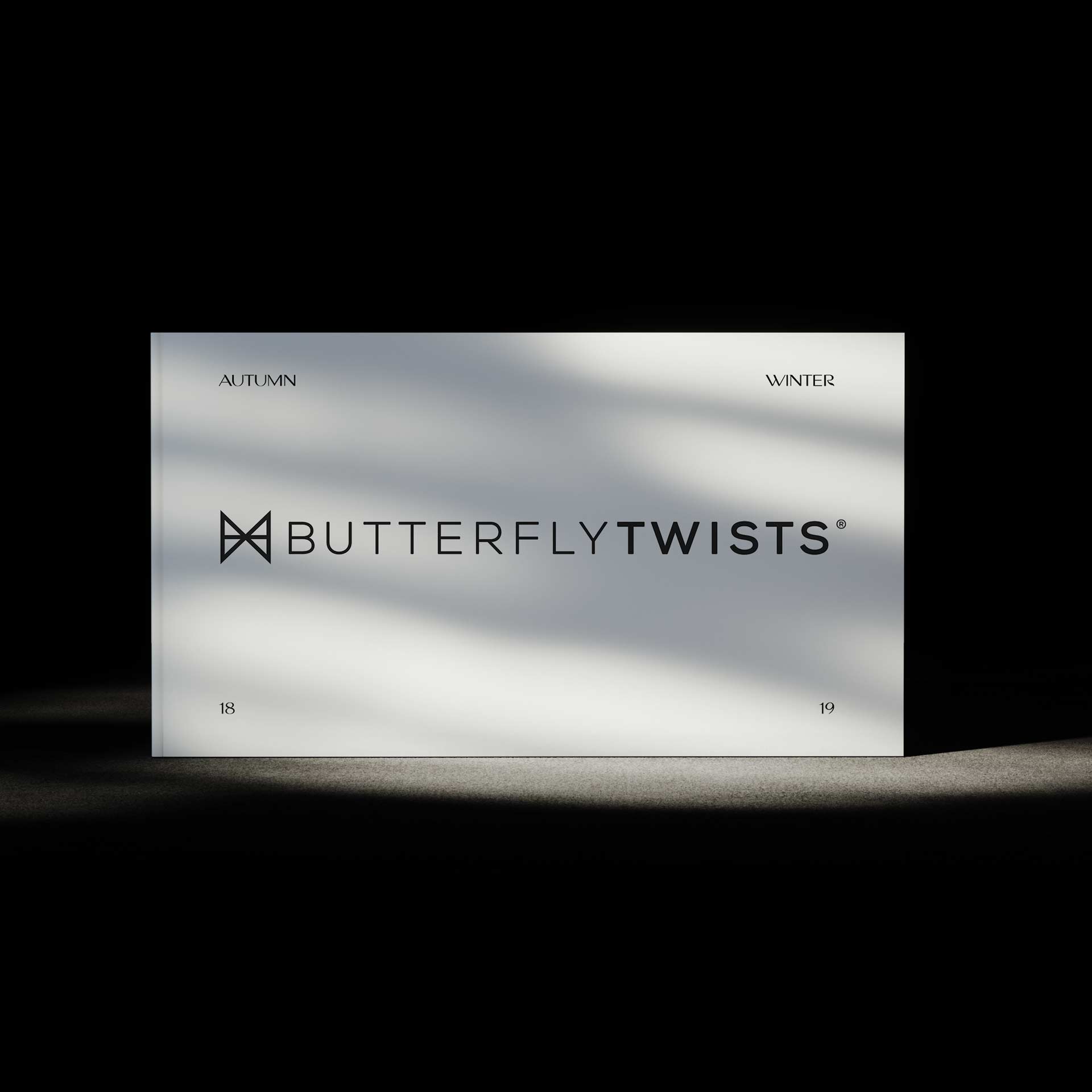 Butterfly Twists lookbook cover: Clean, minimalist design with logo, 'AUTUMN'/'WINTER' flanking it. '18'/'19' at bottom corners. Spotlight effect, modern simplicity, seasonal transition.