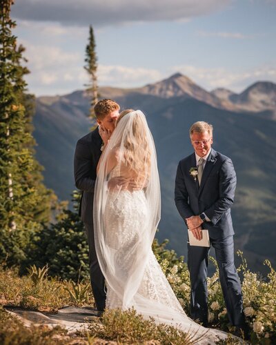 The couple kiss during their ceremony as the officiant smiles beside them.