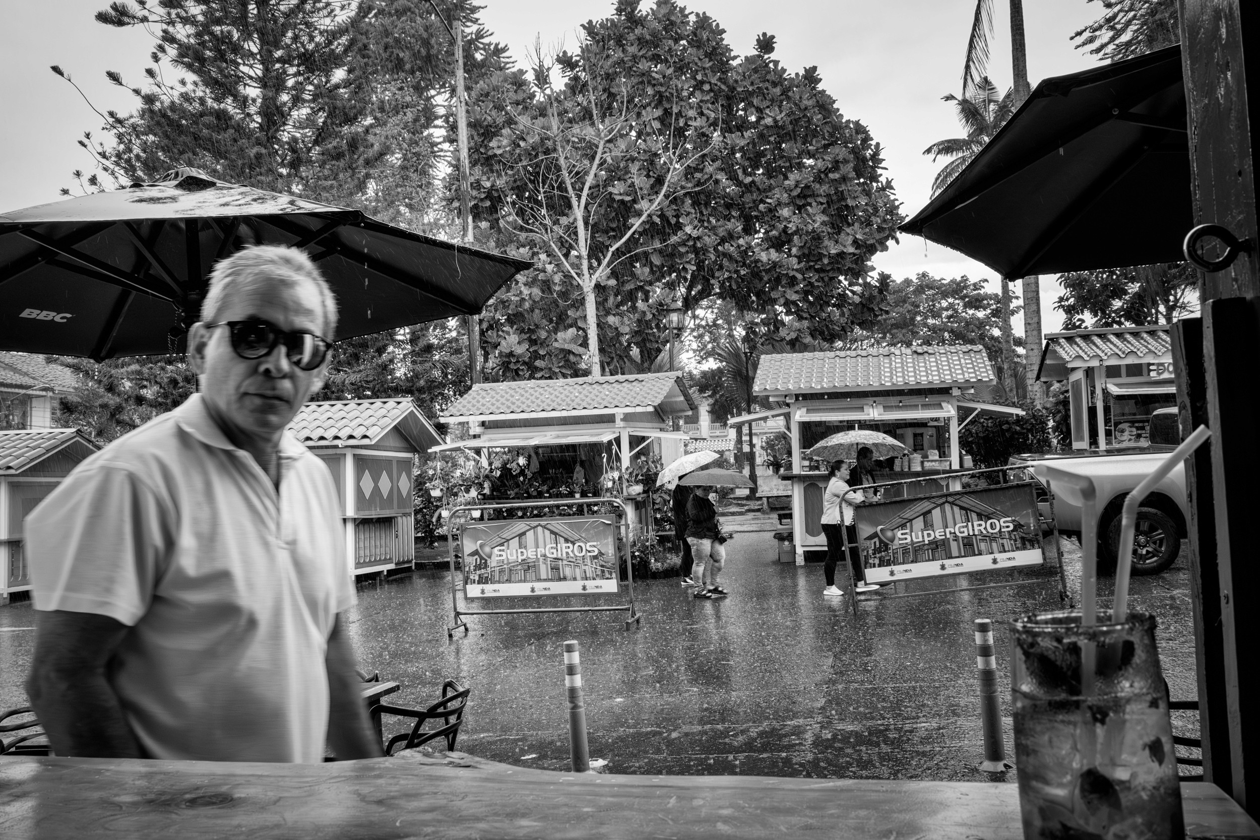 Rainy street scene with people passing by a bar window.