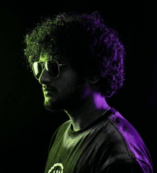 Profile of Co-Founder Gnanesh MJ, featuring curly hair and sunglasses, lit by dramatic neon colors.