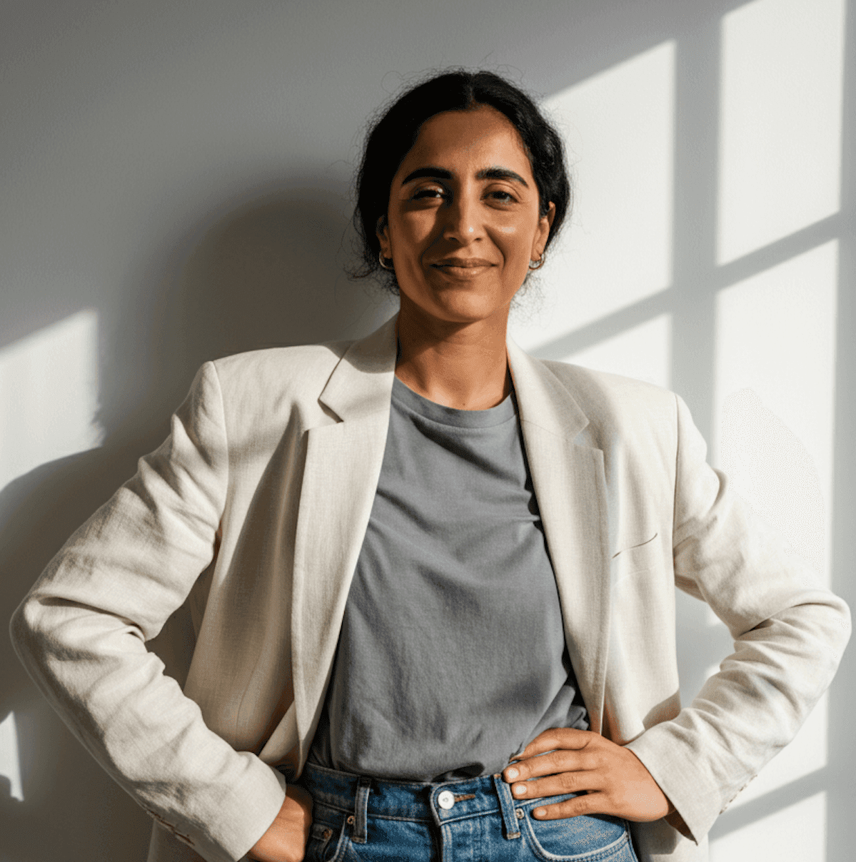 A woman dressed in a white blazer and jeans stands by a window, creating a stylish and professional appearance.