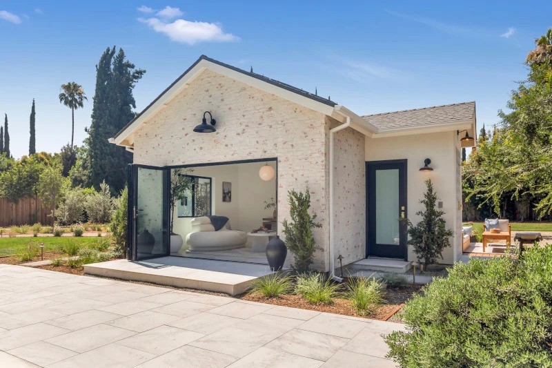 A modern house with a light exterior, front porch, and landscaped yard, set against a blue sky.