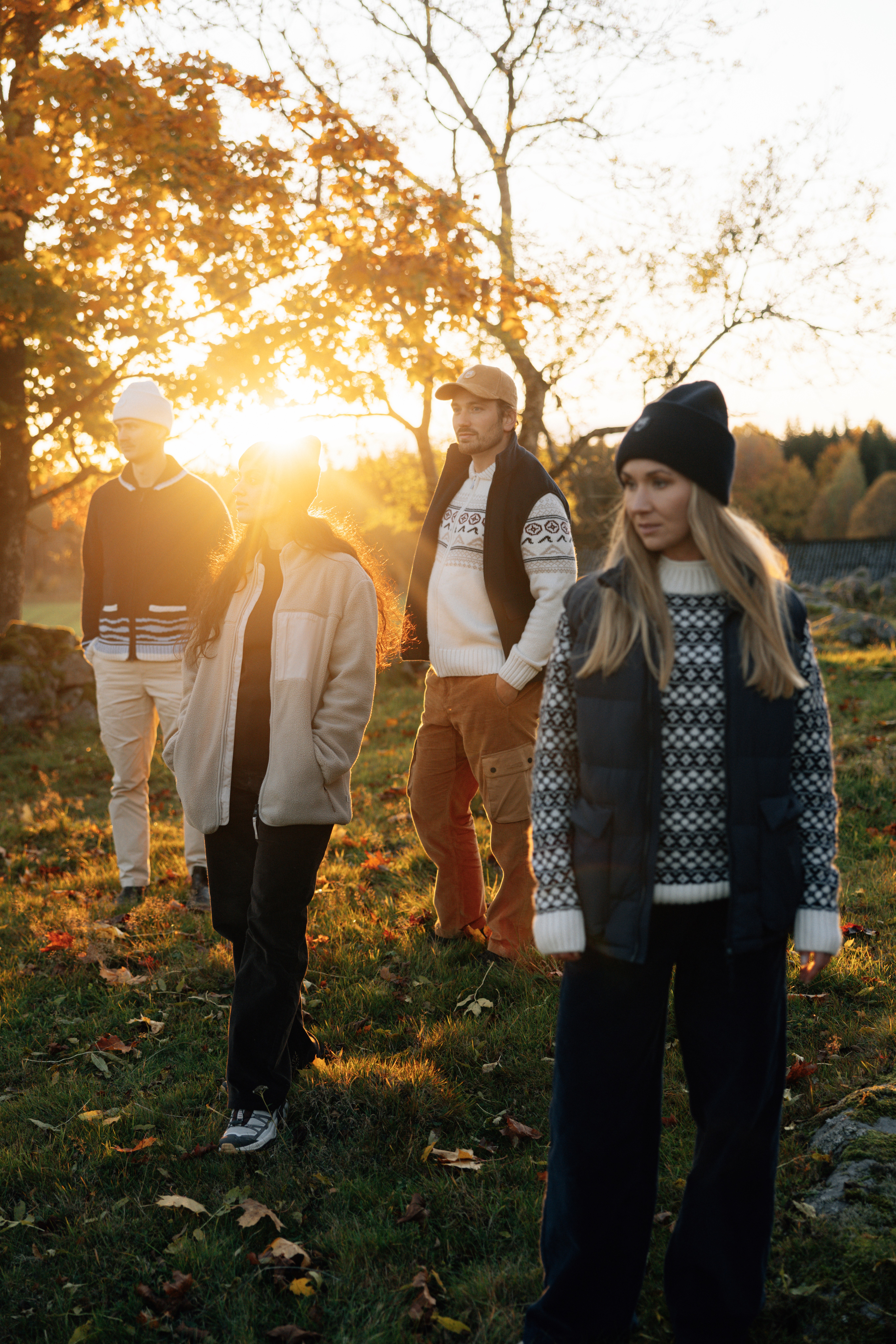 4 amis posent devant un soleil d'automne couchant, vêtus de pulls d'hiver et de bonnets