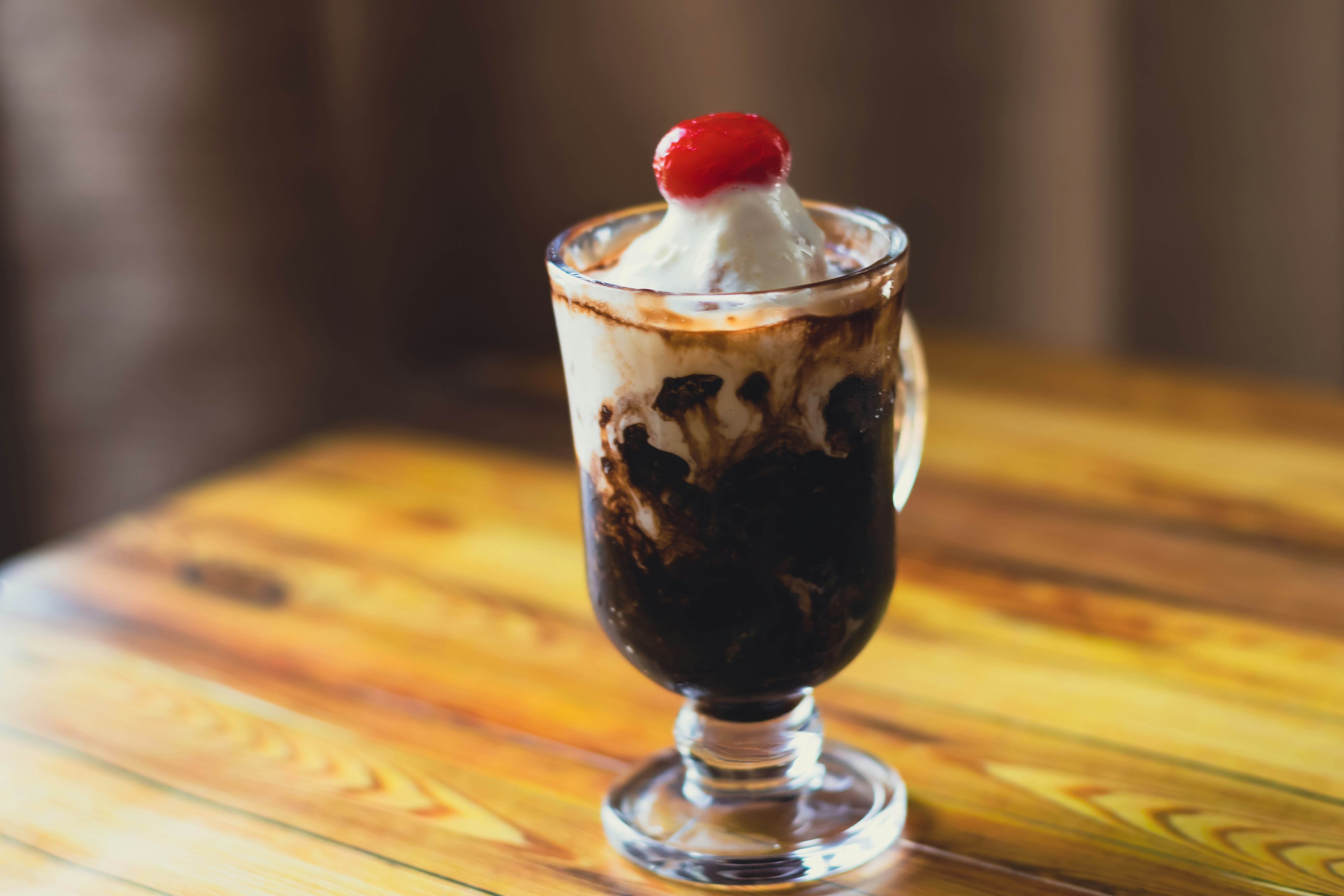 A hot fudge sundae in a tall glass topped with whipped cream and a cherry