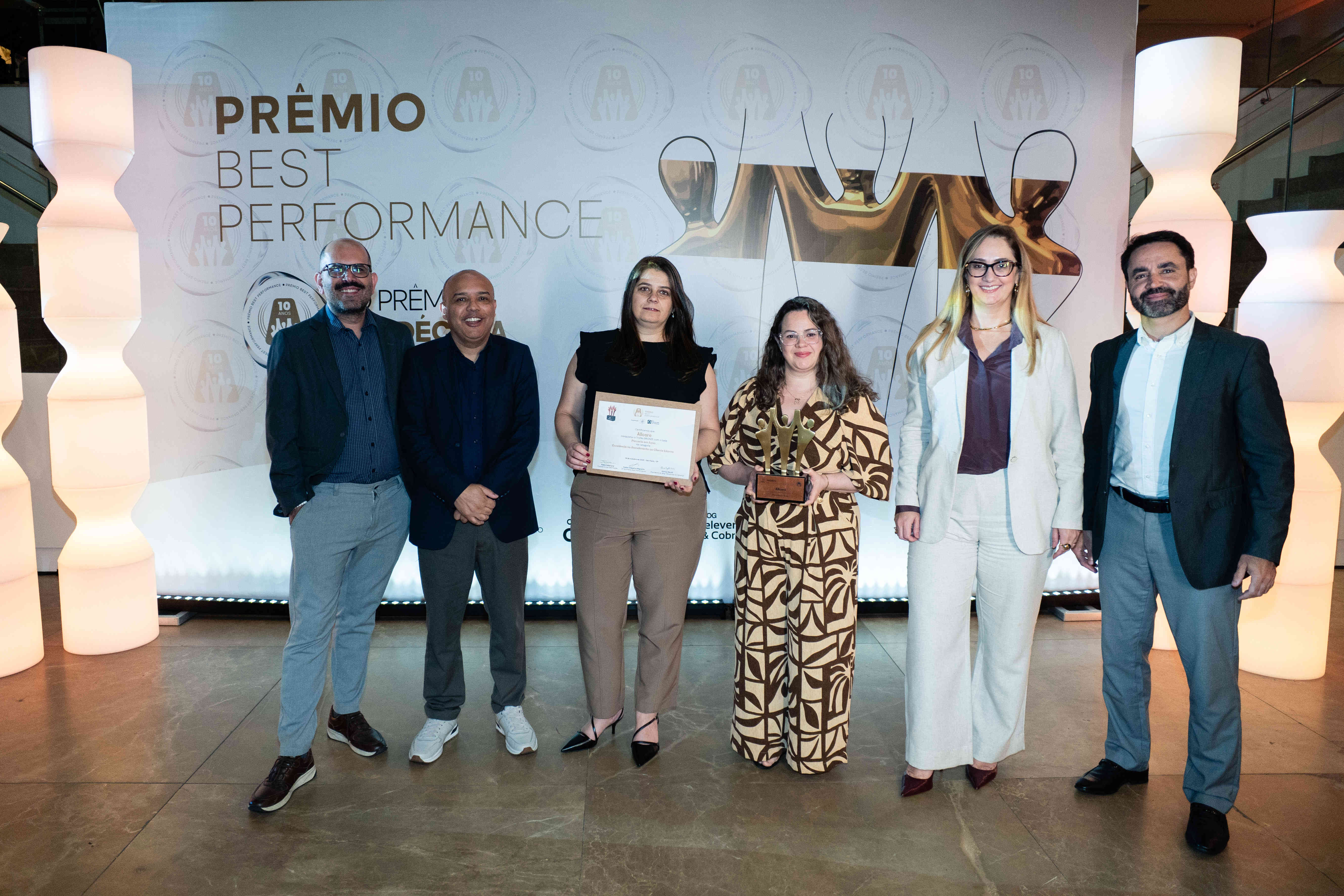 Executivos da Allcare posando com troféu bronze e certificado no palco do Prêmio Best Performance 2025